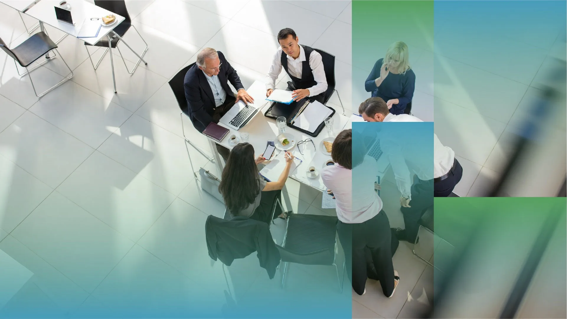 Overhead view of several people seated around a small round table in a bright office space, working with laptops, documents, notebooks, and coffee cups, with abstract blue and green graphic overlays partially framing the scene.