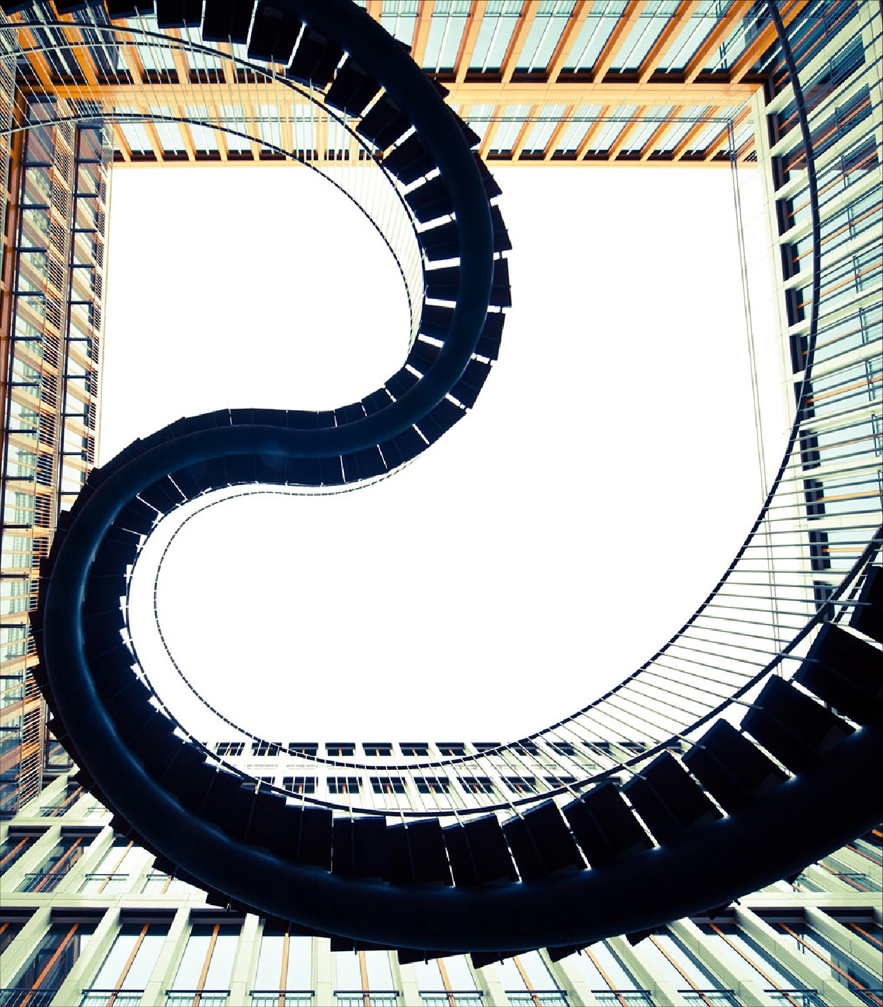 Upward view of a spiral staircase framed by glass and steel architecture